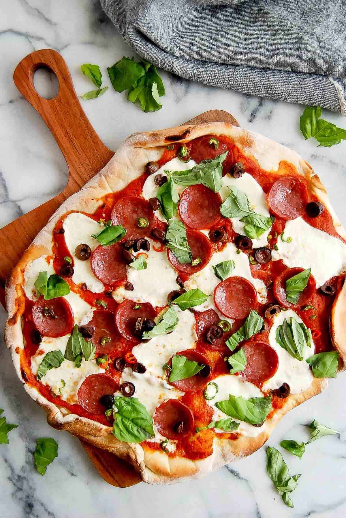 spicy diavola pizza with hot salami on cutting board, with basil on top.