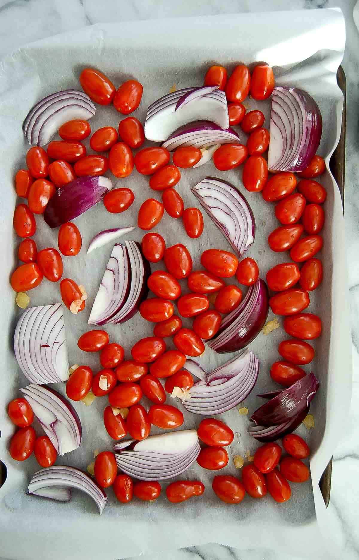 grape tomatoes, red onion wedges and garlic on sheet pan.