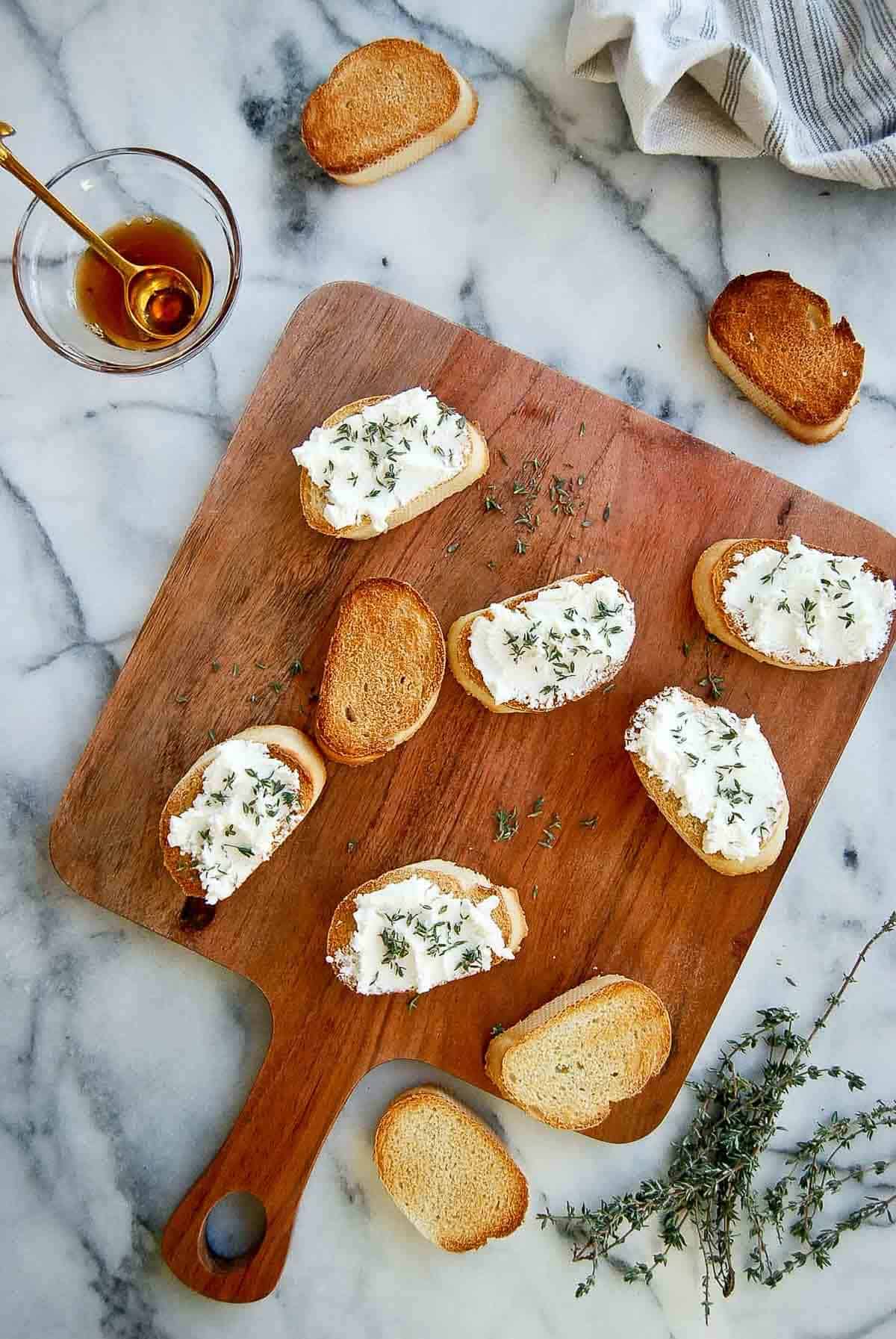 sliced baguette with goat cheese spread and sprinkled thyme on serving board.