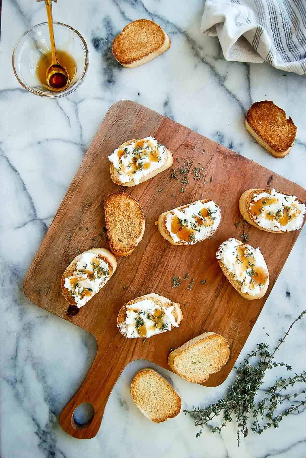 goat cheese crostini with thyme and honey on cutting board.