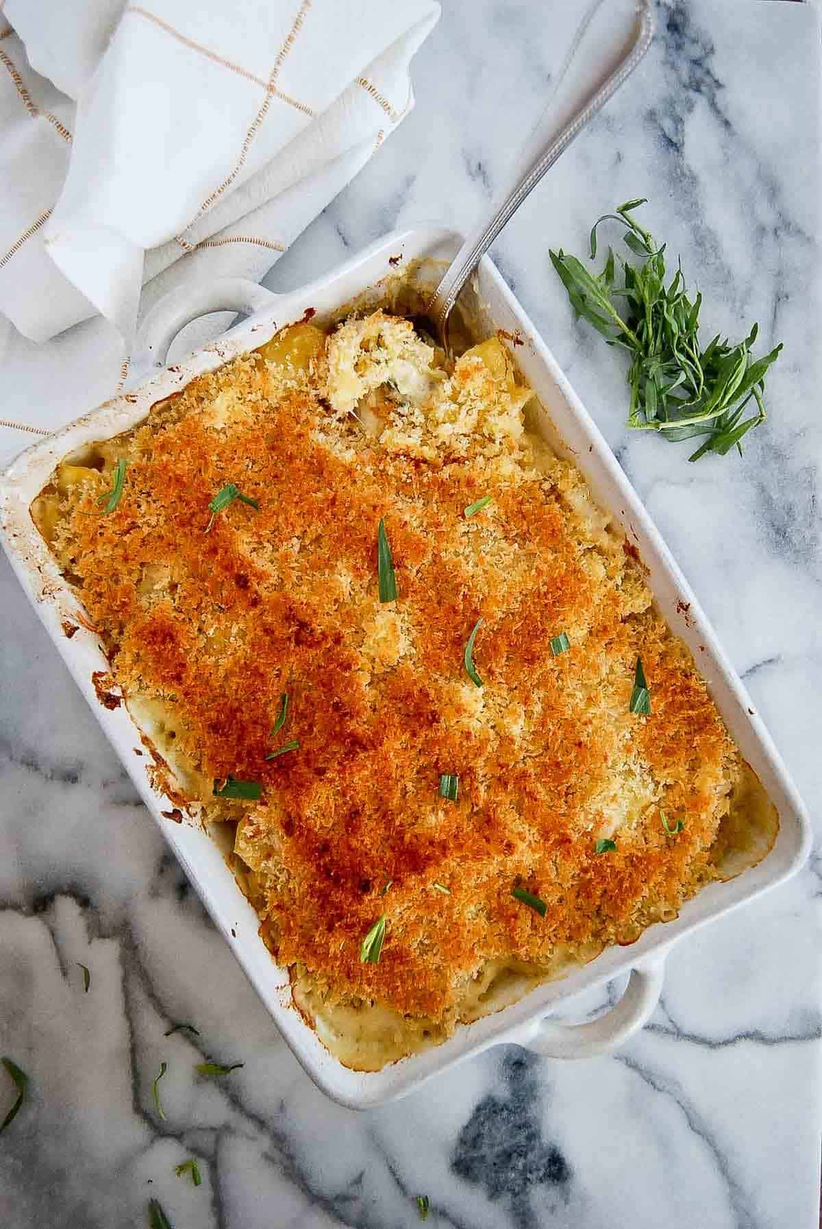 creamy instant pot scalloped potatoes with panko breadcrumb topping in baking dish with serving spoon inserted.