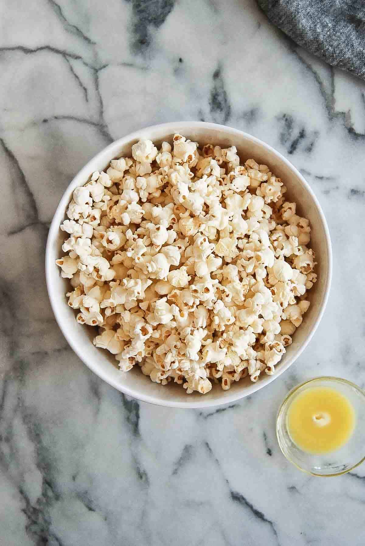 bowl of popped popcorn with bowl of melted butter next to it.