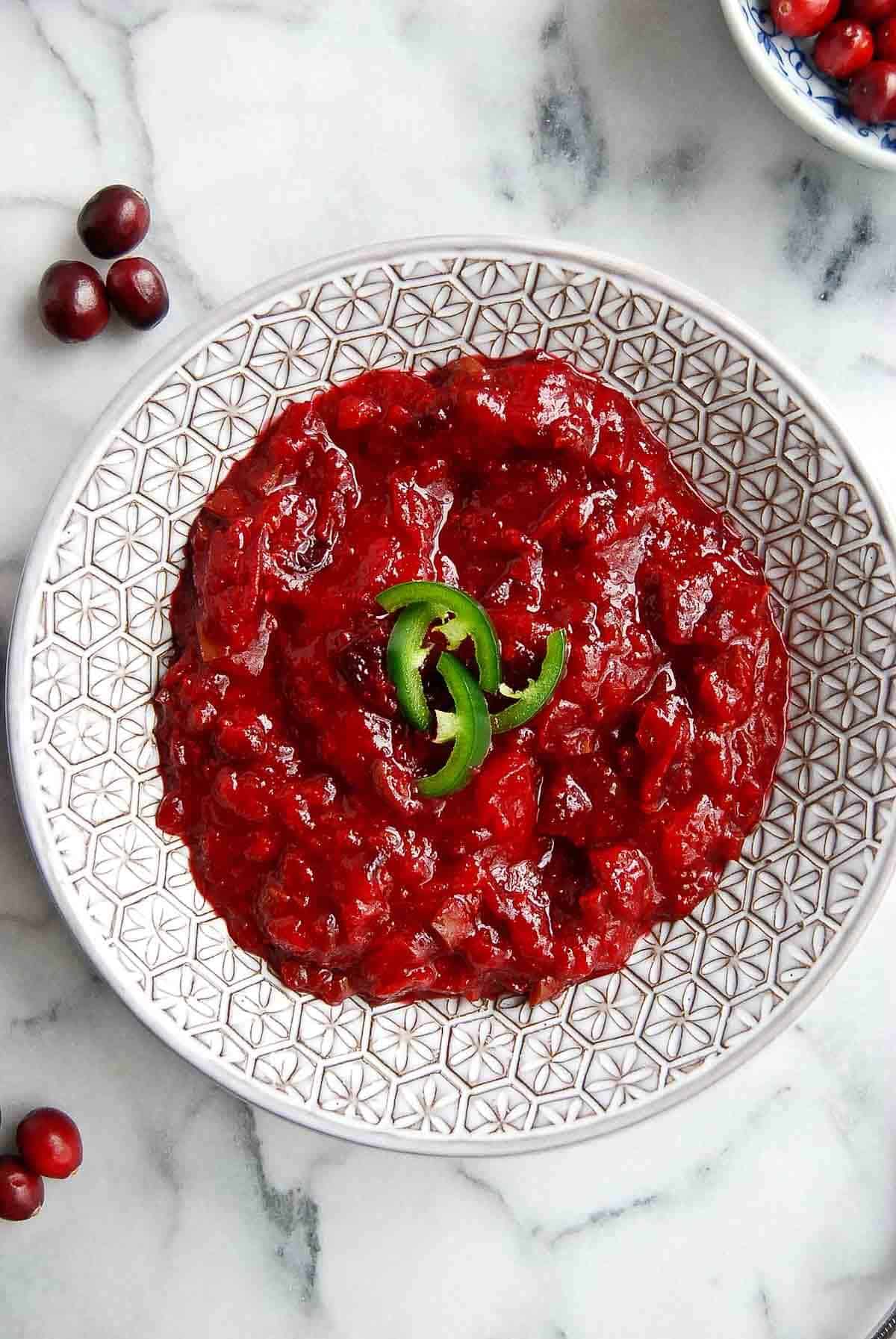 jalapeno cranberry sauce in bowl with fresh jalapenos on top.