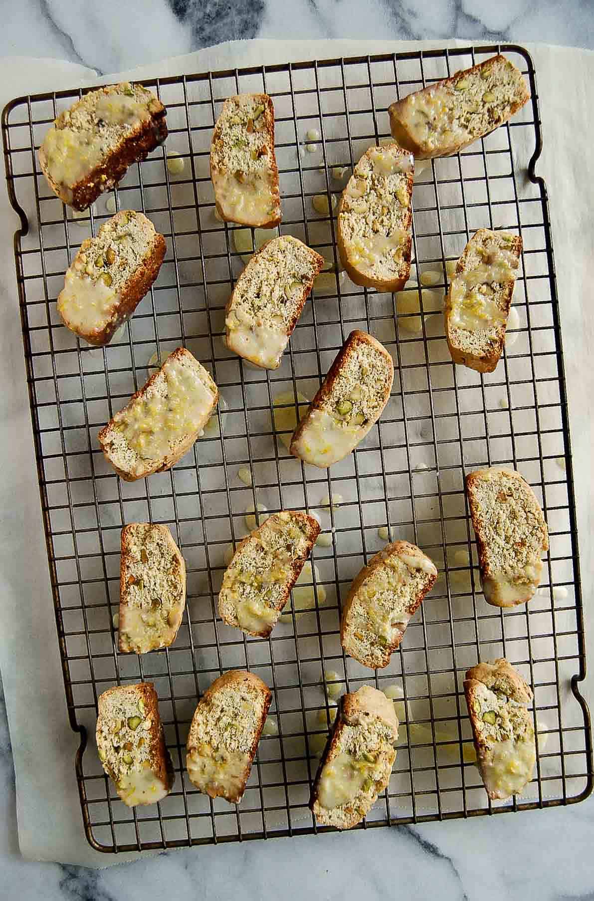 lemon glazed lemon biscotti cookies with pistachios on cooling racks.