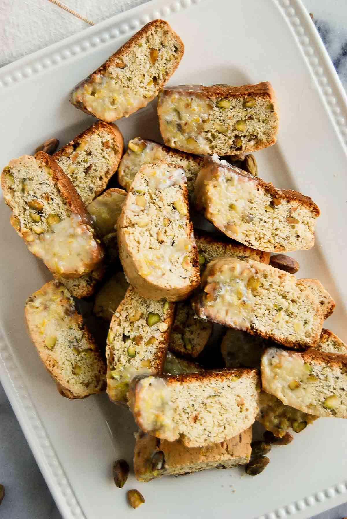 close up of lemon biscotti cookies with pistachio and lemon glaze on plate.