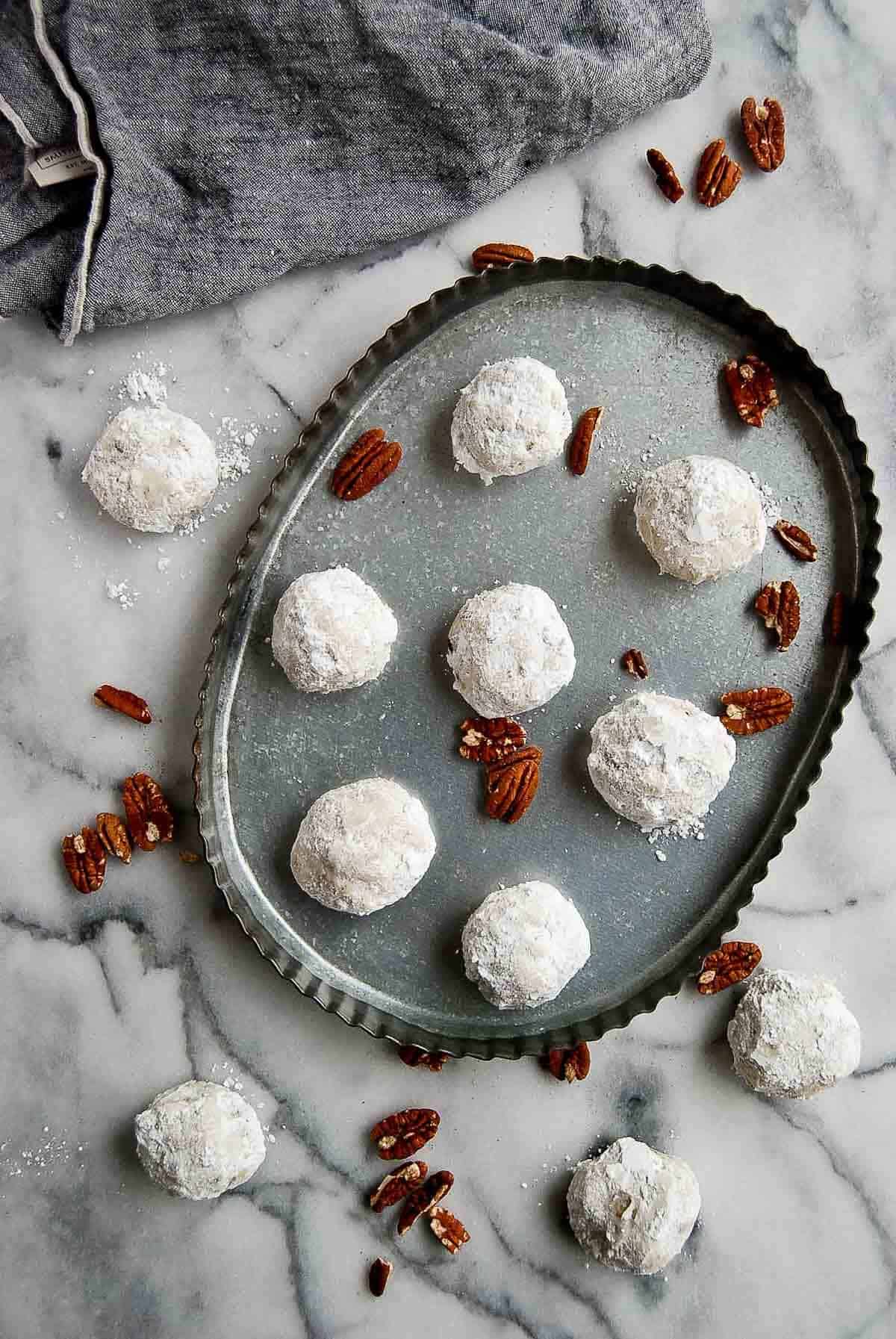 baked mexican cookies on platter with pecans scattered around.