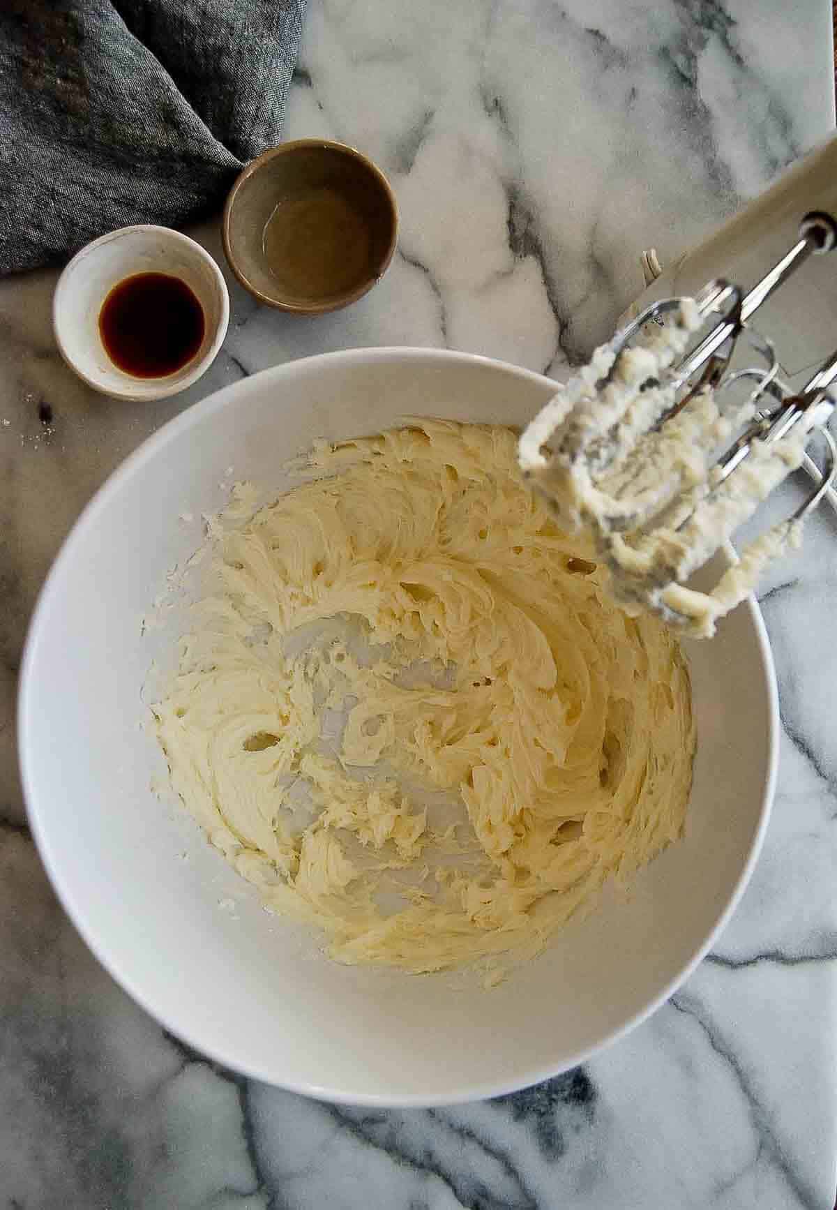 Creamed butter and powdered sugar in bowl with electric mixer to the side.