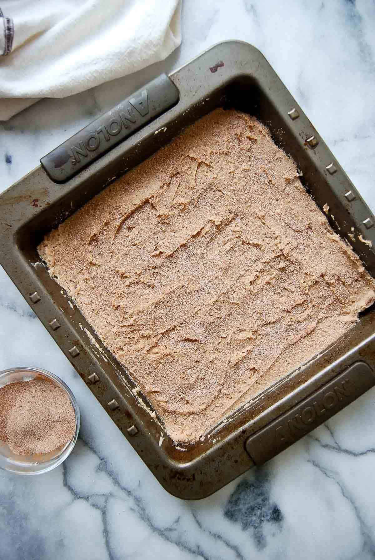 snickerdoodle dough in baking pan with cinnamon sugar sprinkled on top.