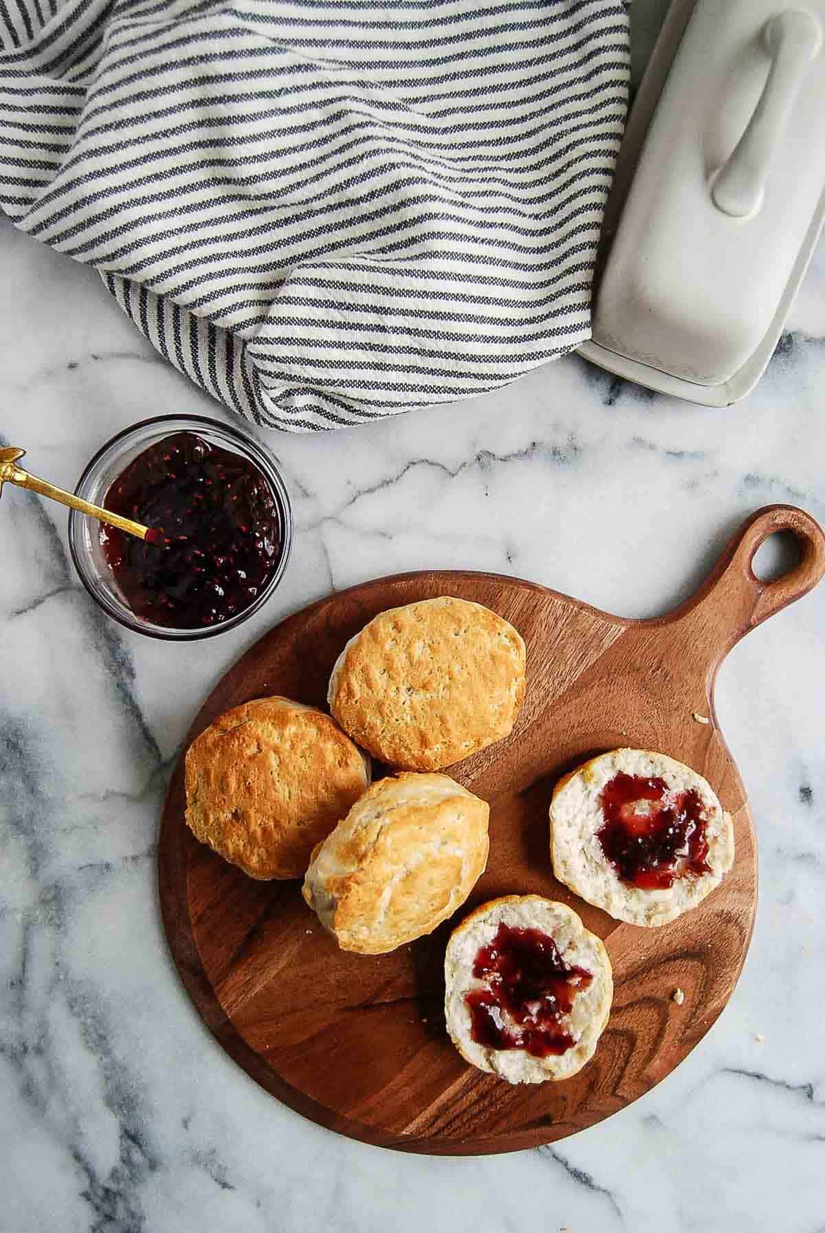 cutting board with pillsbury grand biscuits on top, and one cut open with butter and jelly.