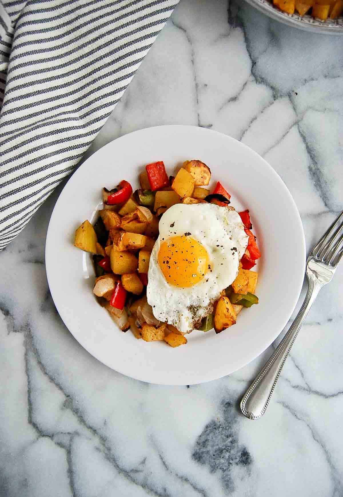 plate of air fryer breakfast potatoes with fried egg on top.