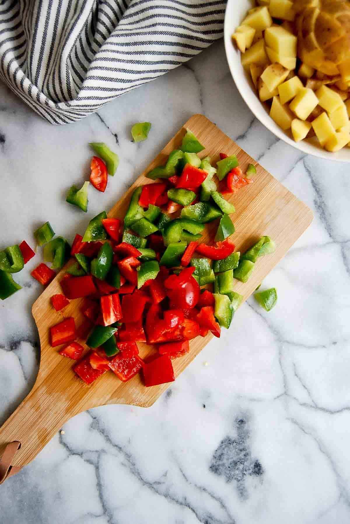 diced red and green pepper on cutting board, with bowl of diced potatoes on the side.