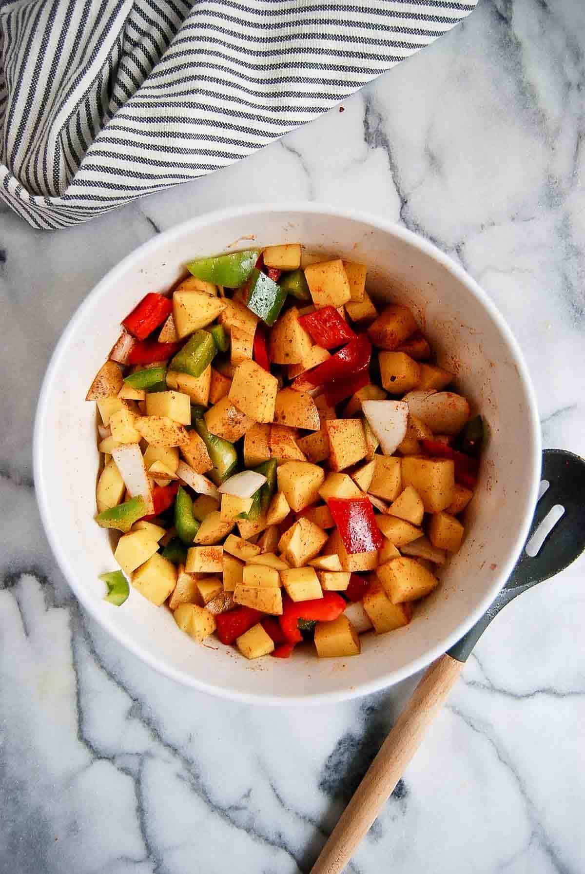 diced potatoes, onion, red and green pepper with spices in bowl.