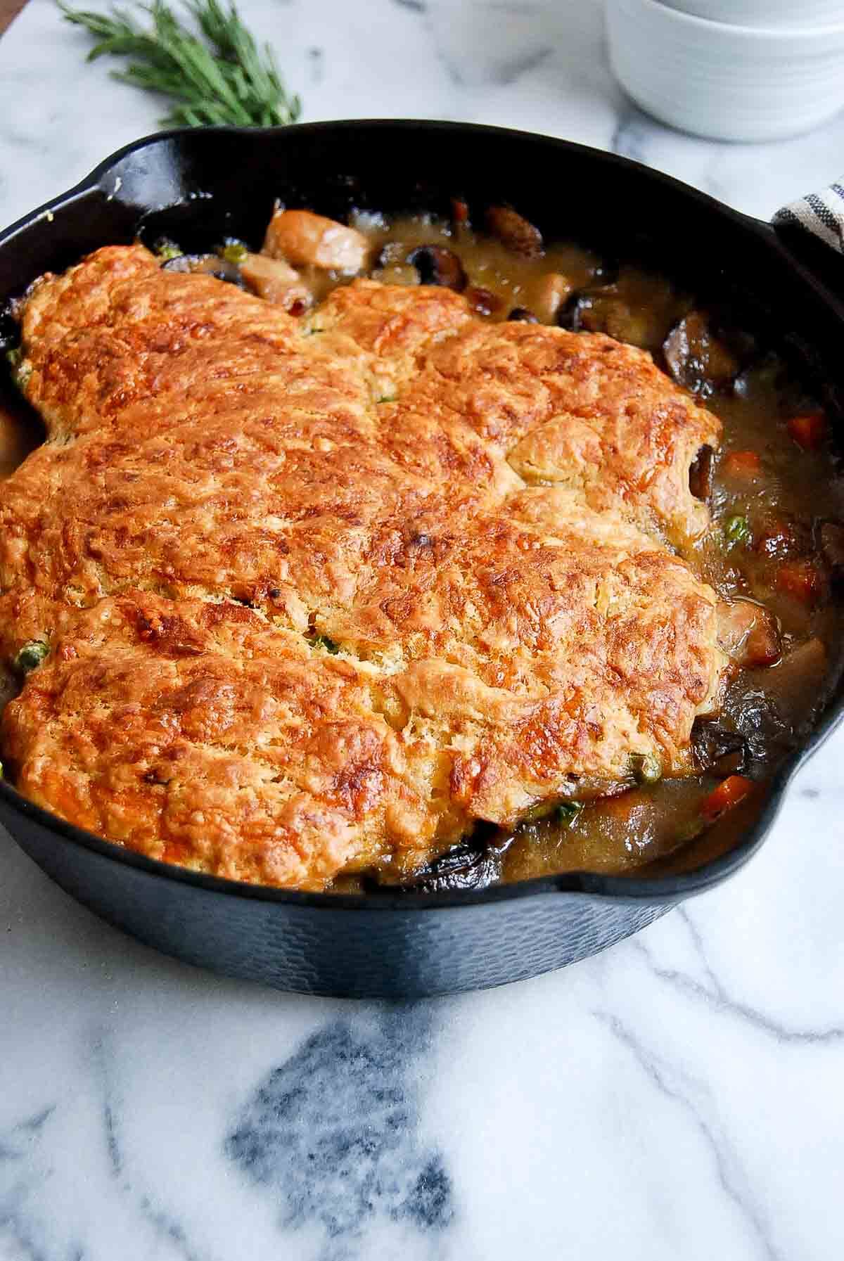 side view of chicken cobbler with crusty cheddar biscuit topping in skillet.