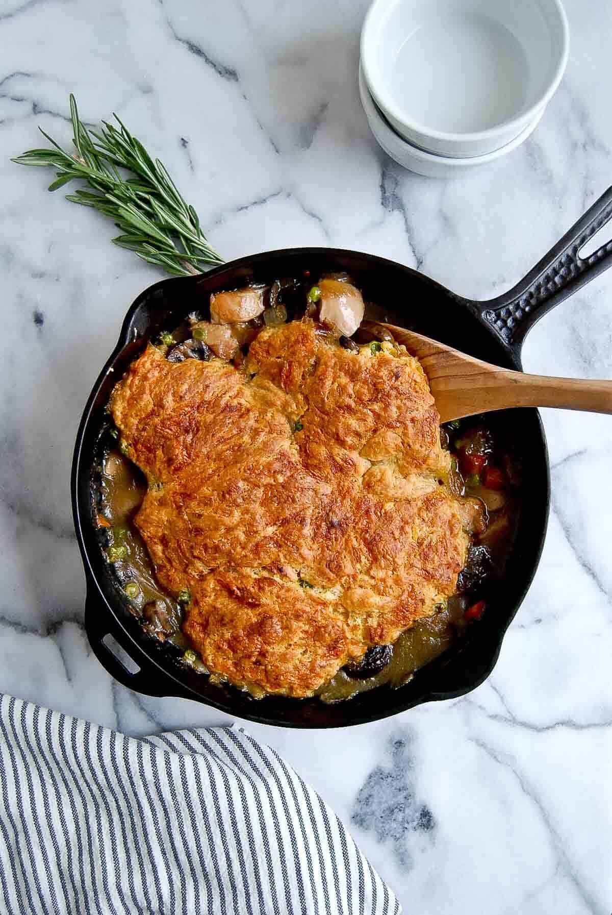 chicken cobbler in skillet with wooden spoon inserted.
