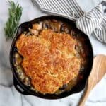 chicken cobbler with cheddar biscuit topping in cast iron skillet with wooden spoon on the side.