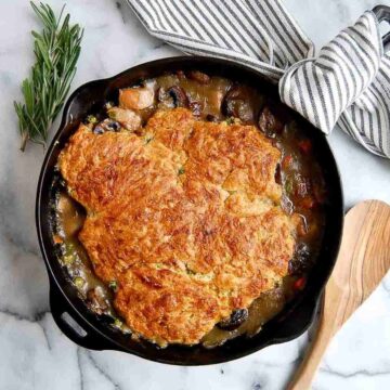 chicken cobbler with cheddar biscuit topping in cast iron skillet with wooden spoon on the side.