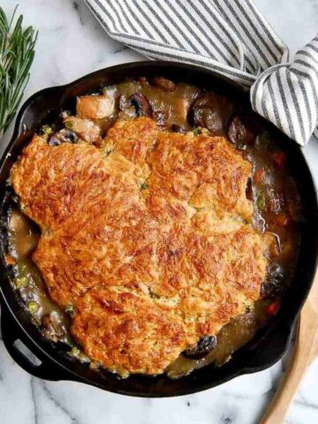 chicken cobbler with cheddar biscuit topping in cast iron skillet with wooden spoon on the side.