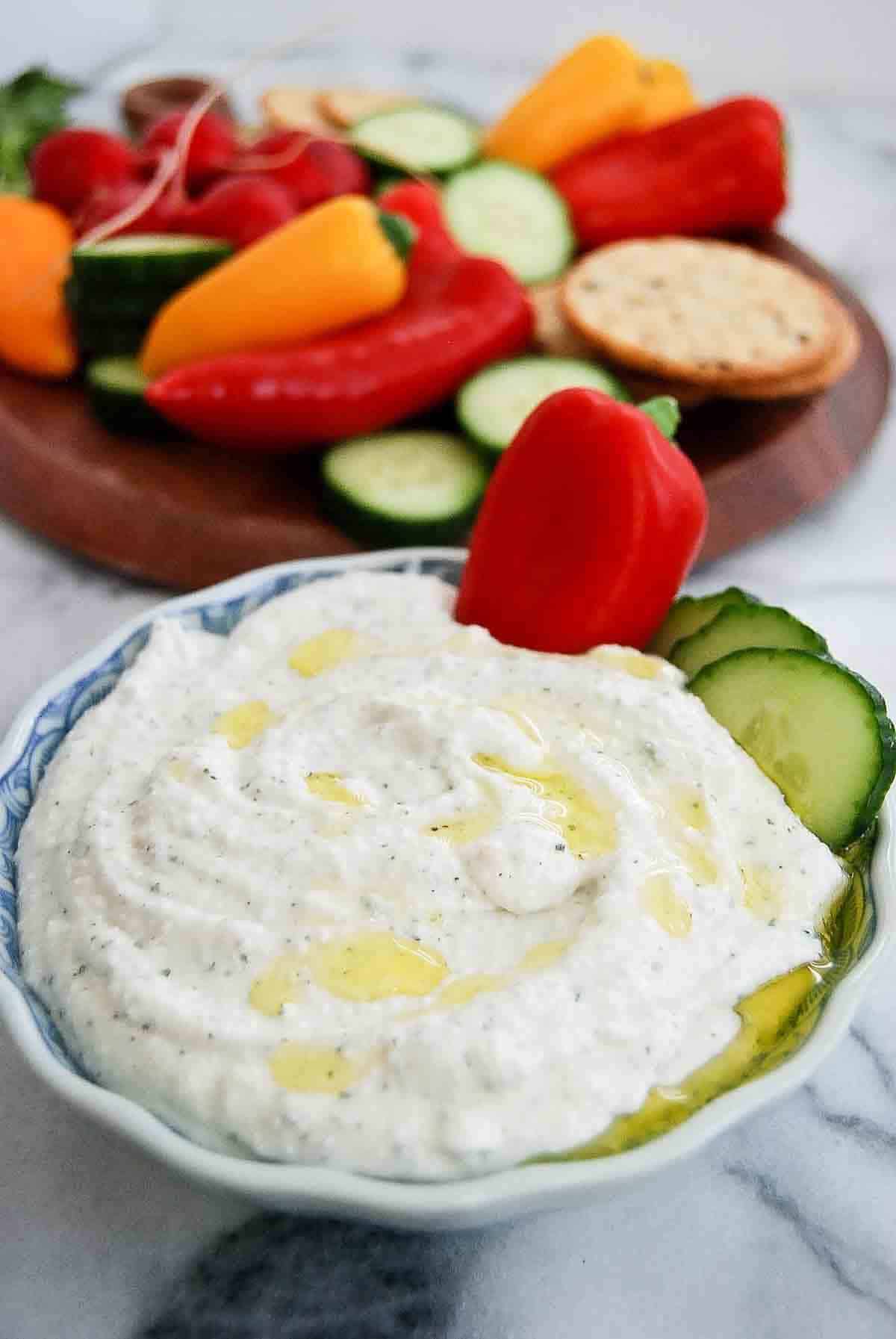 side view of bowl of cottage cheese ranch dip with veggies and crackers in the background.