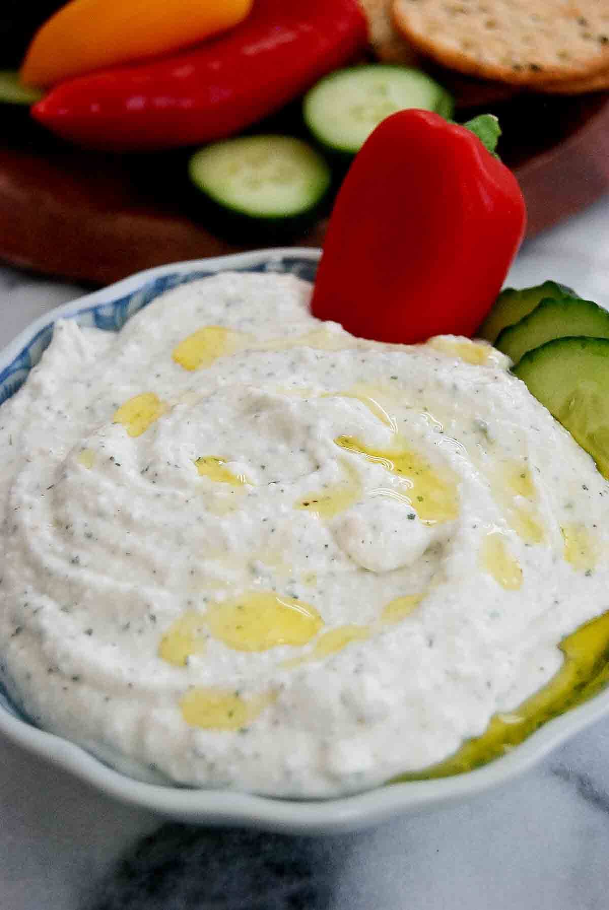 side view of bowl of cottage cheese ranch dip with veggies and crackers in the background.