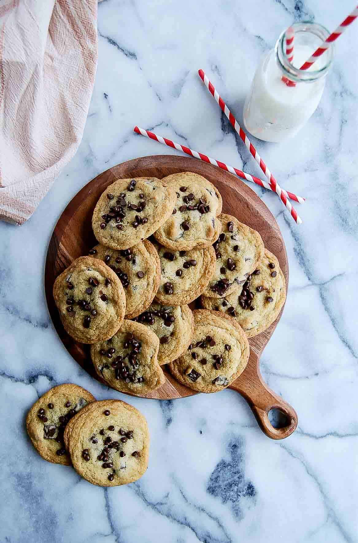 small batch chocolate chip cookies piled onto cutting board with glass of milk to the side.