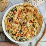 spinach artichoke dip without mayo in bowl with crackers on the side.