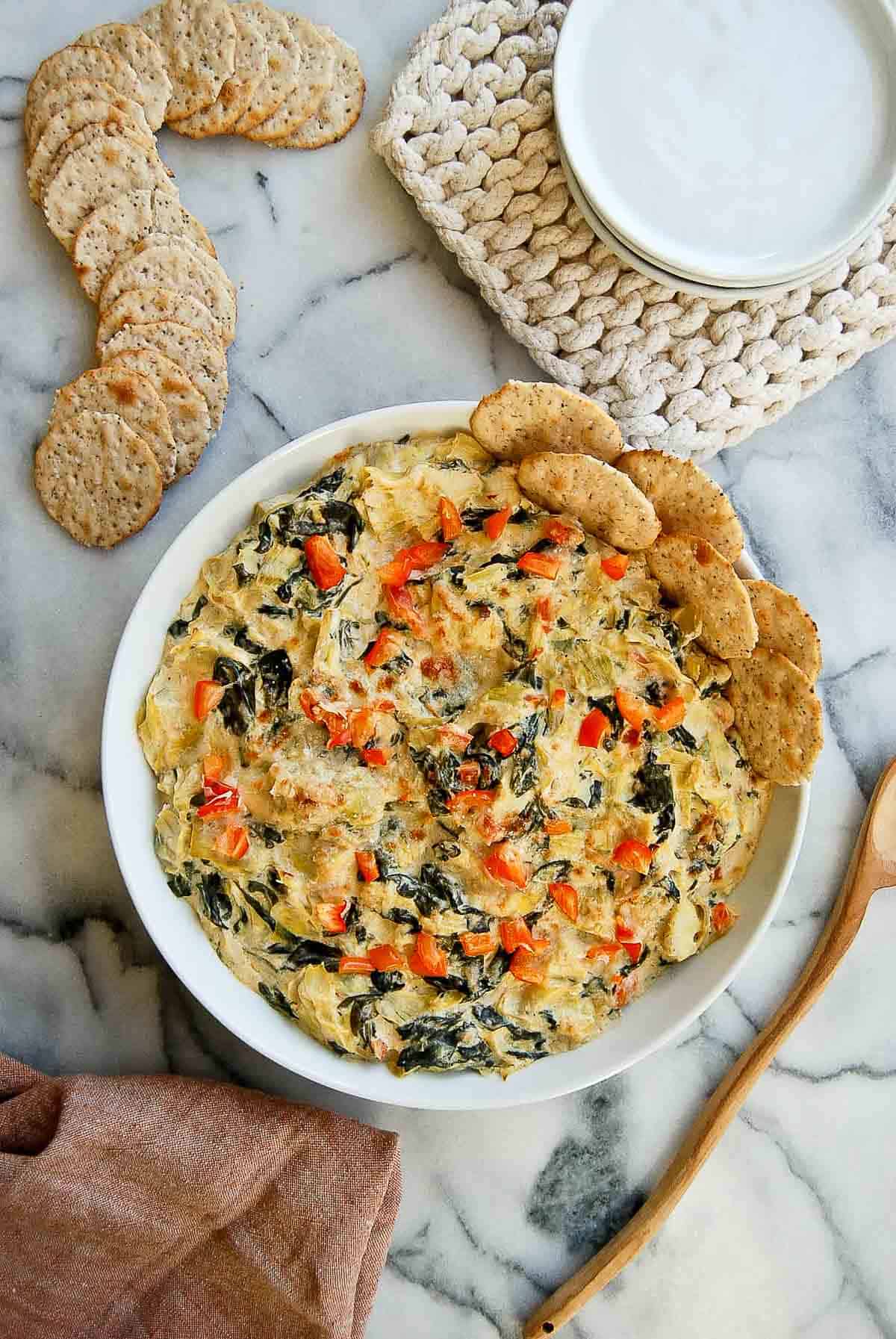 Cooked spinach and artichoke dip without mayo in bowl with crackers on the side.