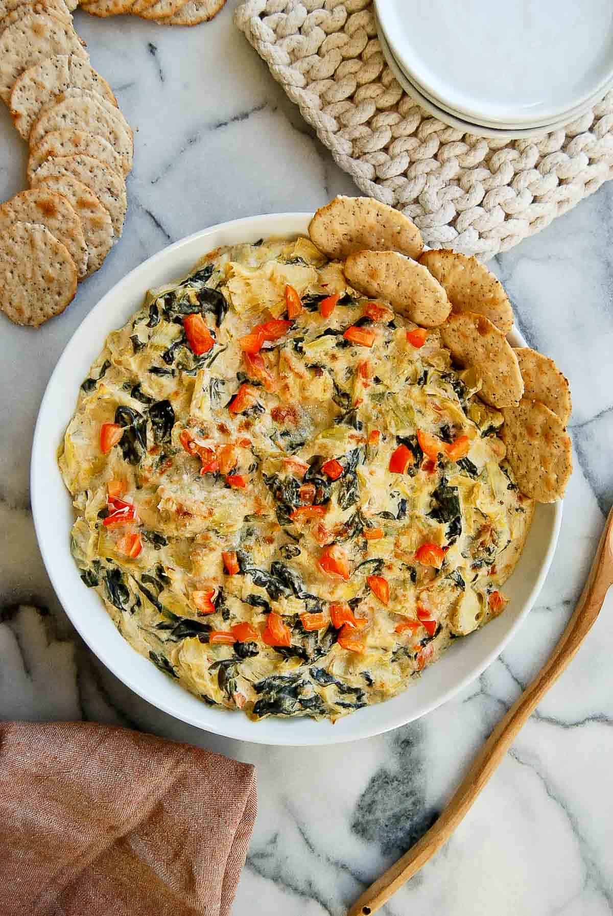 Cooked spinach and artichoke dip without mayo in bowl with crackers on the side.