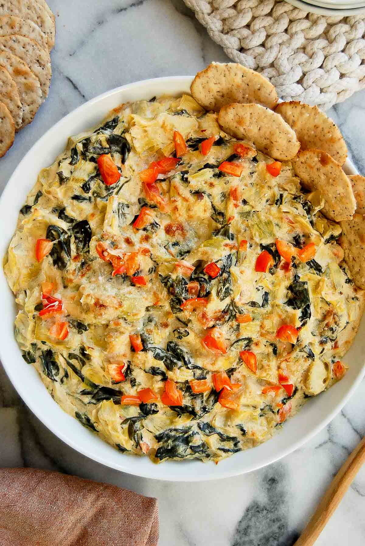 Cooked spinach and artichoke dip without mayo in bowl with crackers on the side.