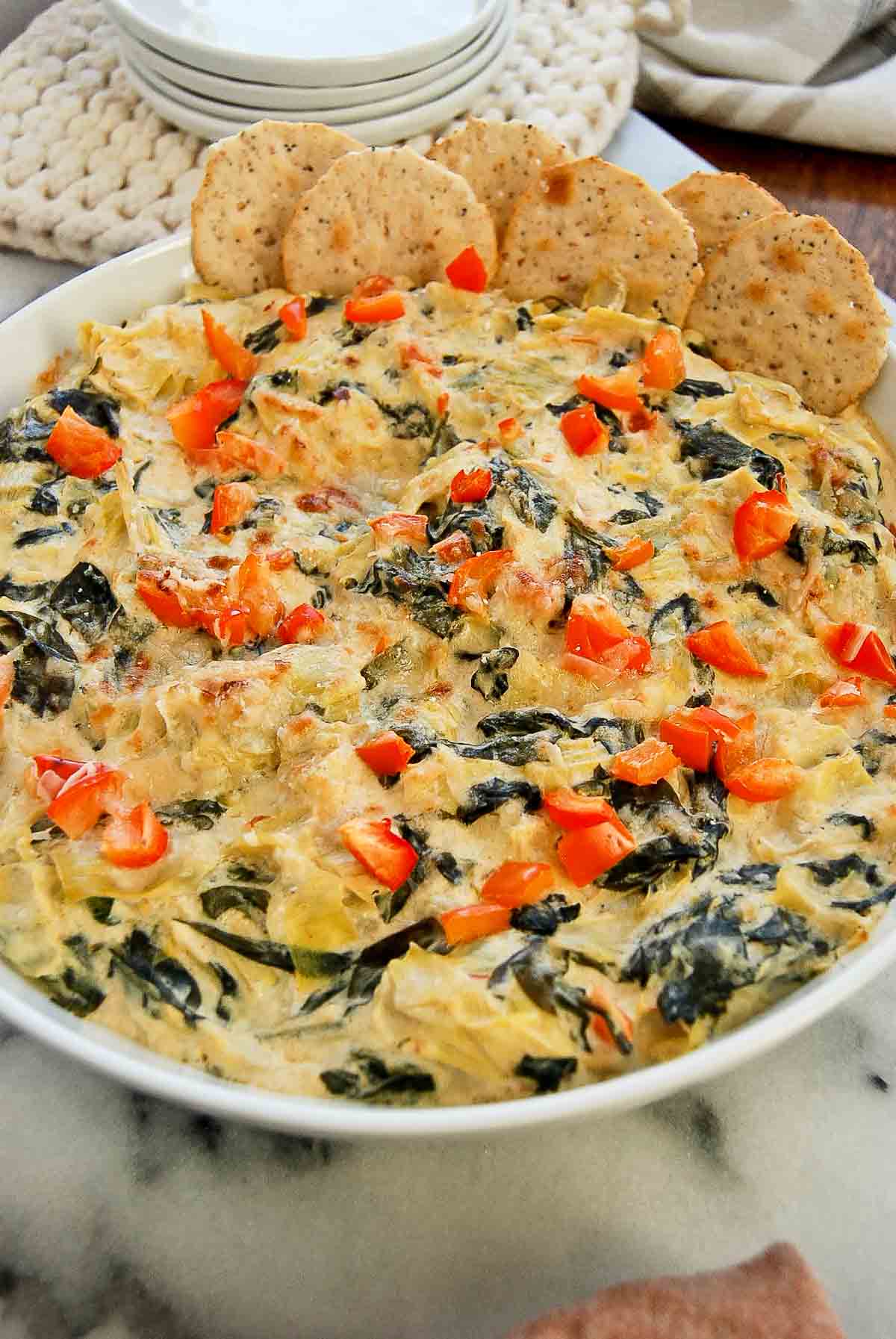 side view of cooked spinach and artichoke dip without mayo in bowl with crackers on the side.