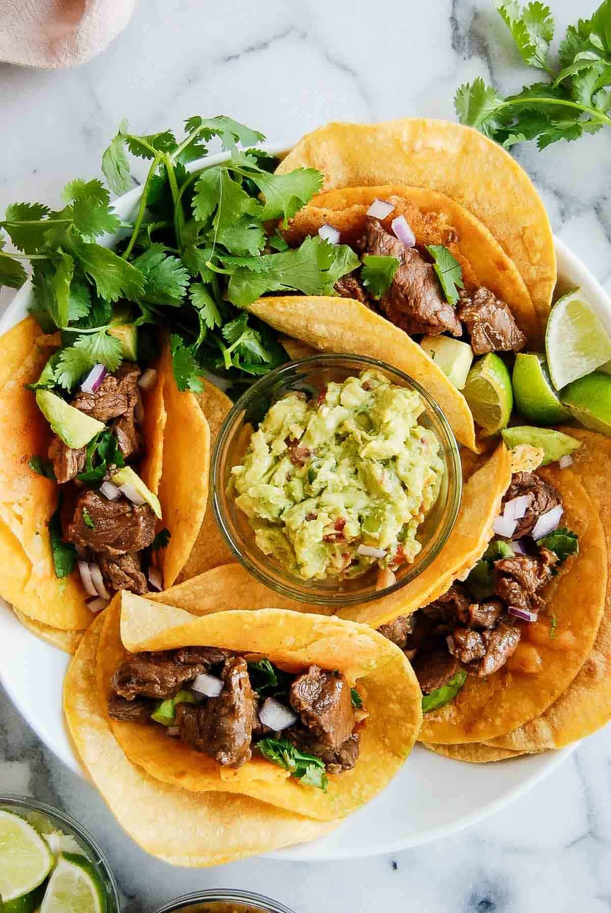 plate filled with carne asada vampiro tacos with bowl of guacamole in the middle.