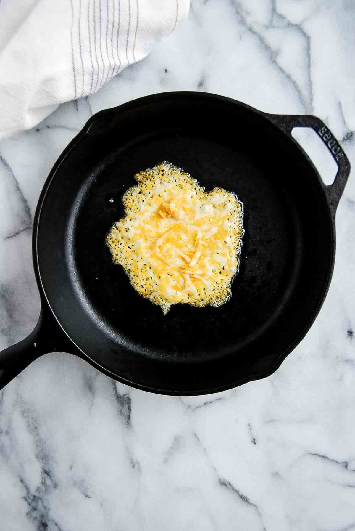 shredded colby jack cheese melting on cast iron skillet.