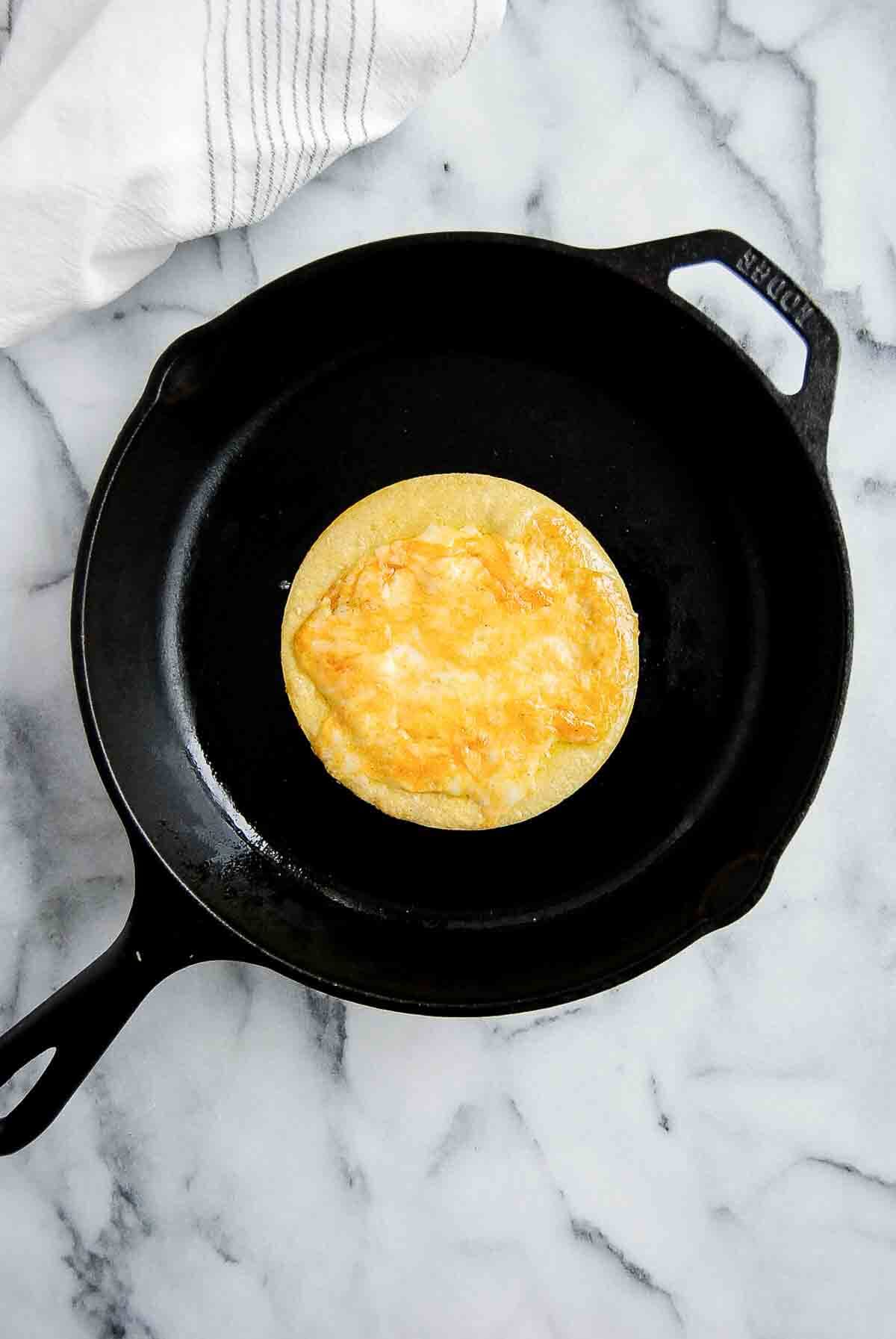 corn tortilla grilling on skillet topped with melted cheese.