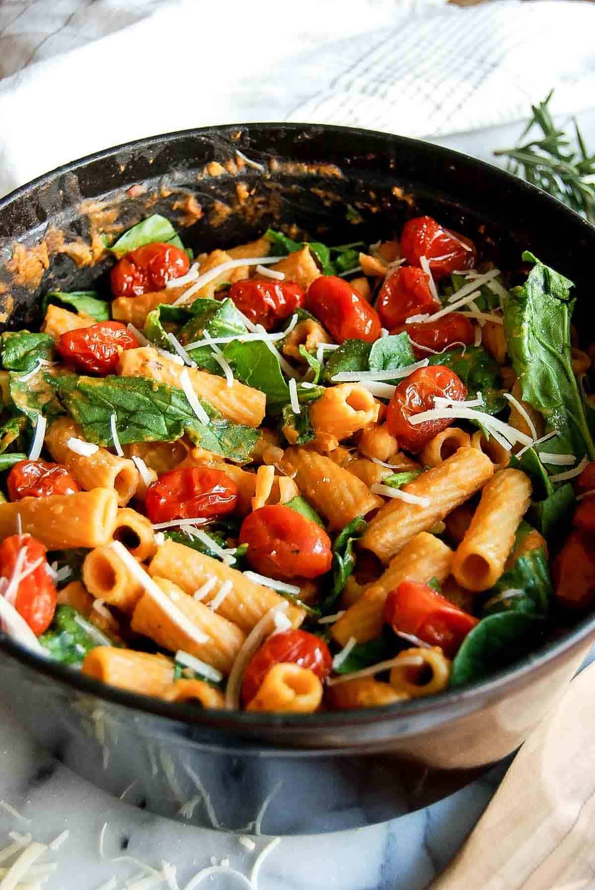 side view of pasta e ceci with spinach and tomatoes on countertop.