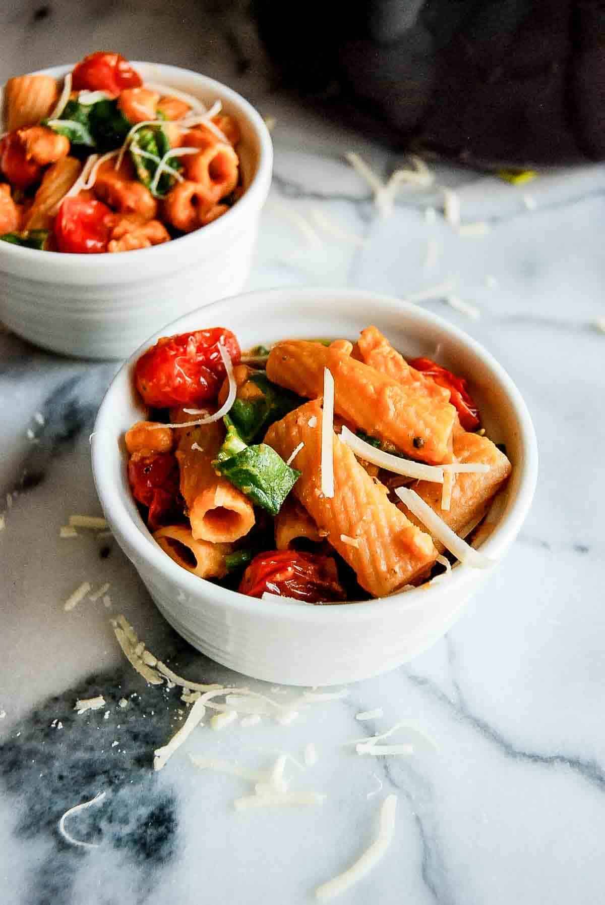 side view of individual bowls with pasta e ceci, spinach and tomatoes on countertop.