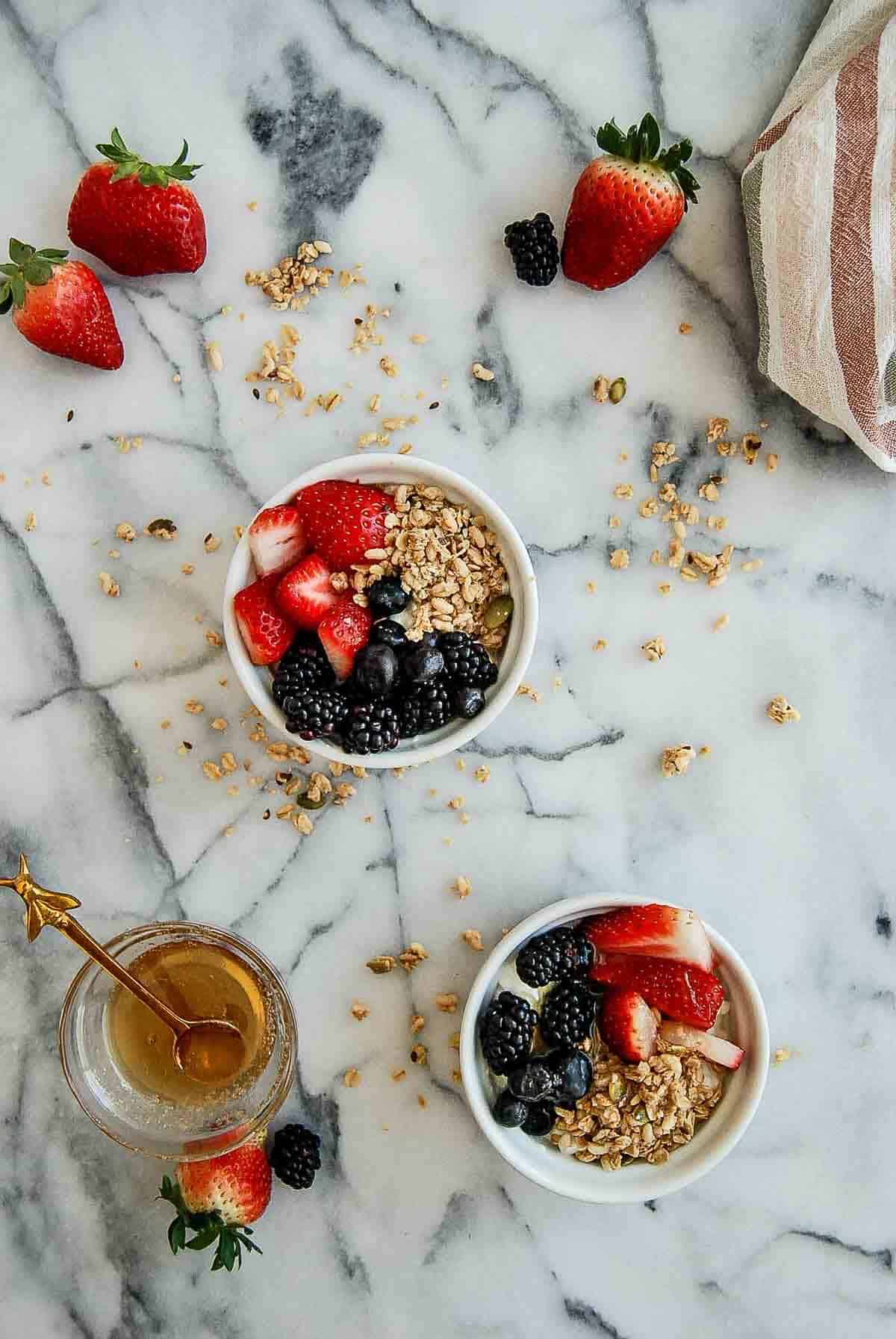 2 cottage cheese with fruit breakfast bowls on countertop, with honey on the side.