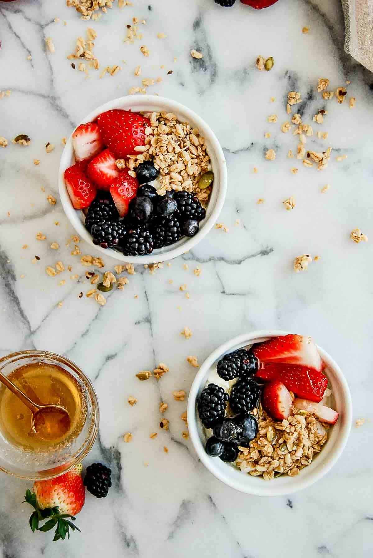 2 cottage cheese with fruit breakfast bowls on countertop, with honey on the side.