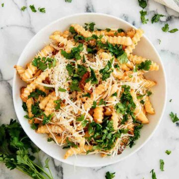 Frozen french fries in the air fryer in bowl with parmesan and parsley.