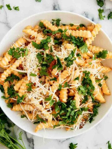 Frozen french fries in the air fryer in bowl with parmesan and parsley.