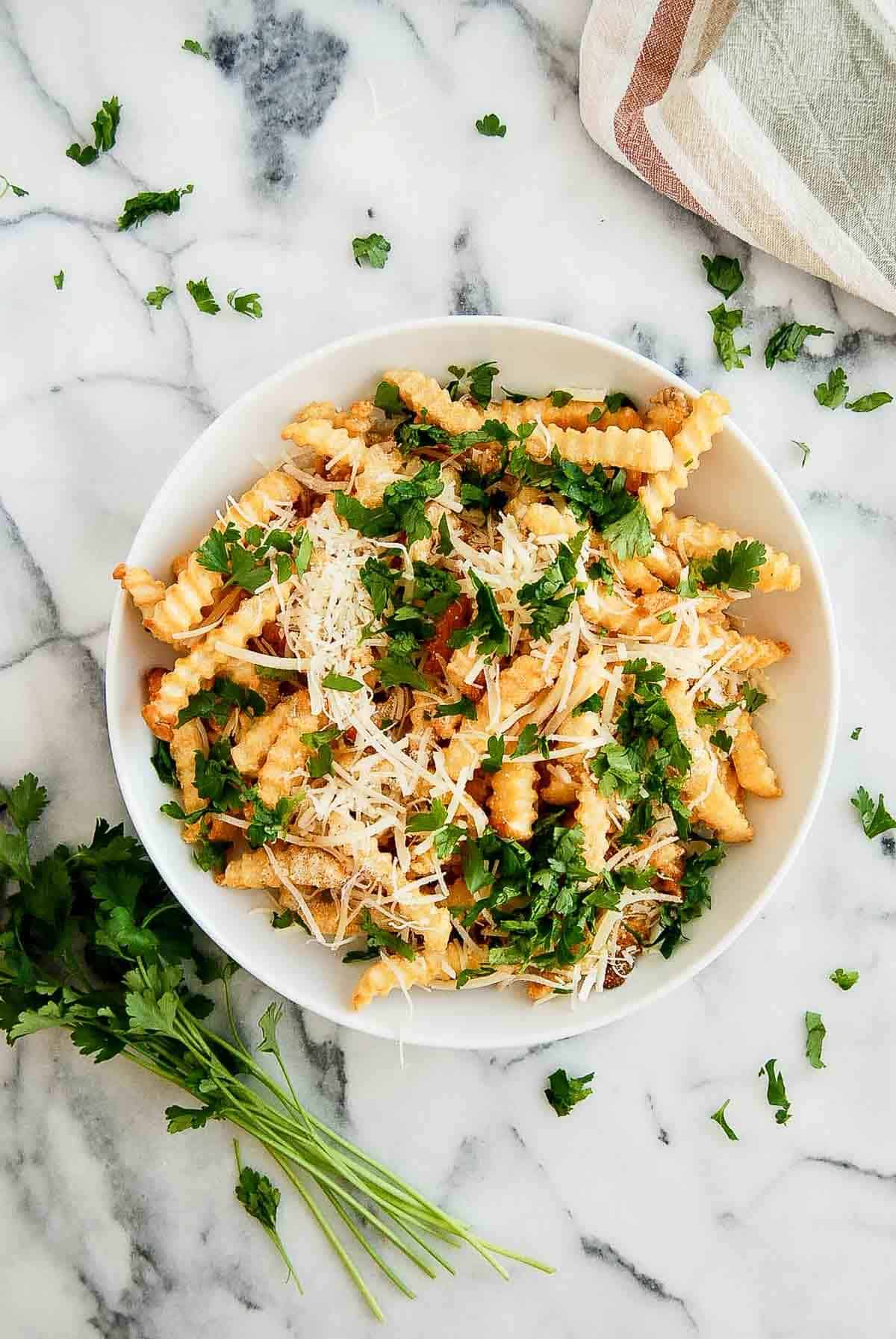 air fryer frozen french fries with garlic salt, parmesan cheese and italian parsley in bowl on countertop.