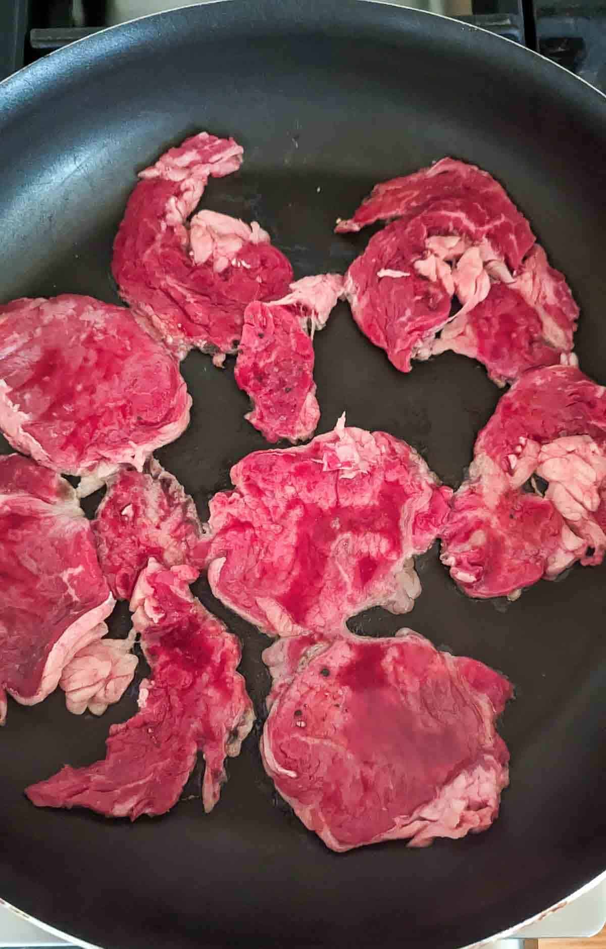 ribeye steak, thinly sliced, in large skillet.