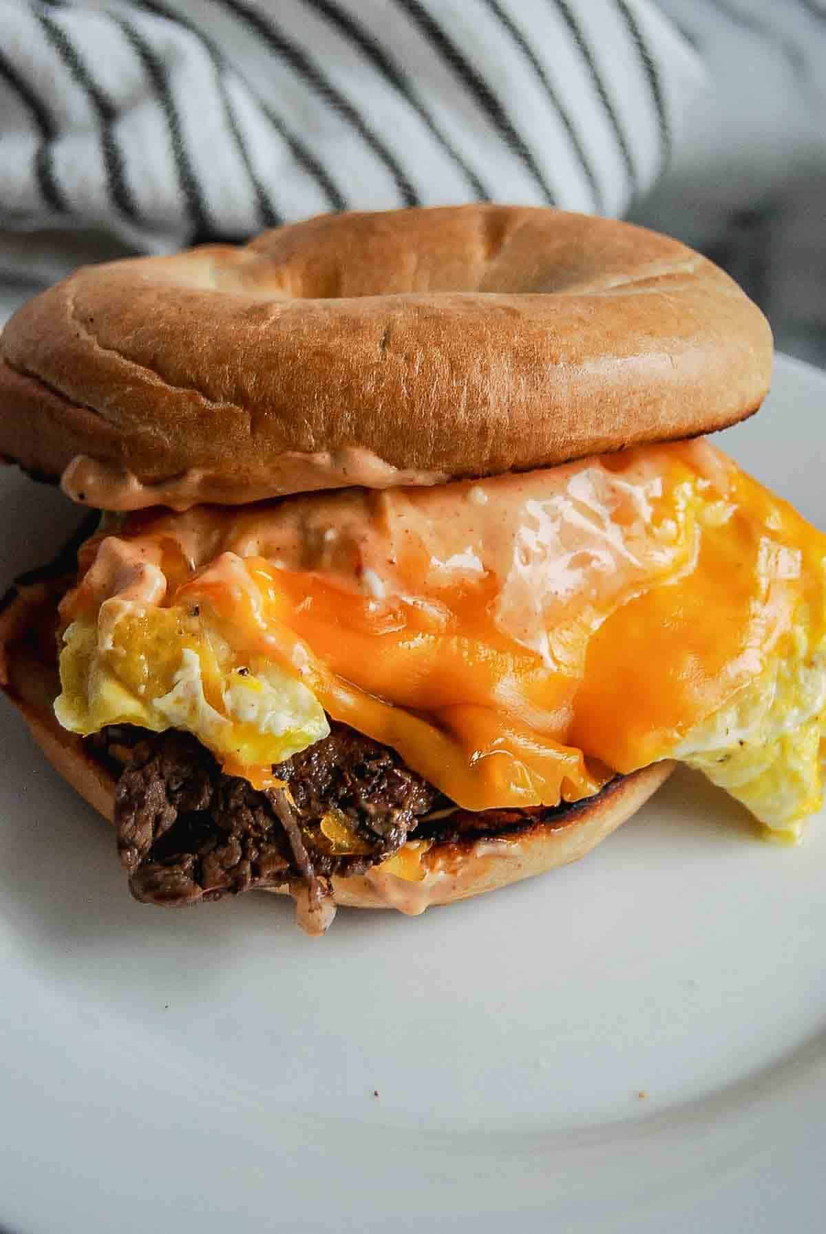 Steak, egg and cheese bagel sandwich on plate.