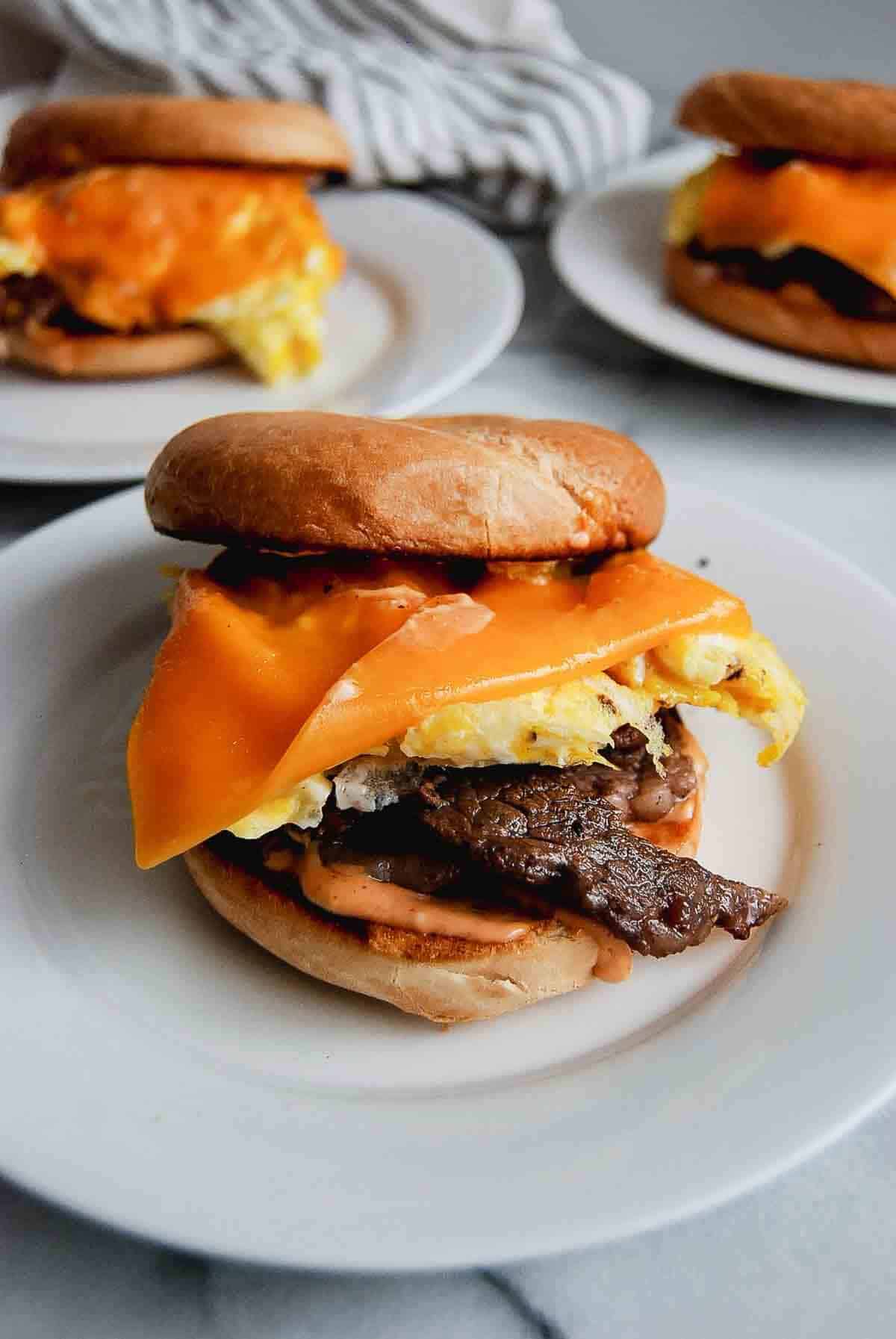 Steak, egg and cheese bagels on plate with breakfast sauce.