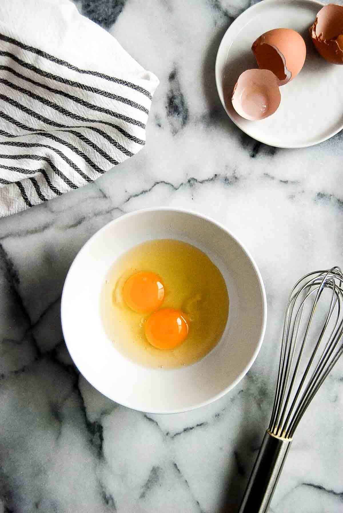 Eggs in bowl with whisk to the side.