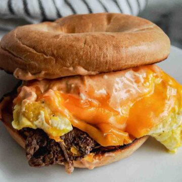 steak egg and cheese bagel with breakfast sauce on plate.