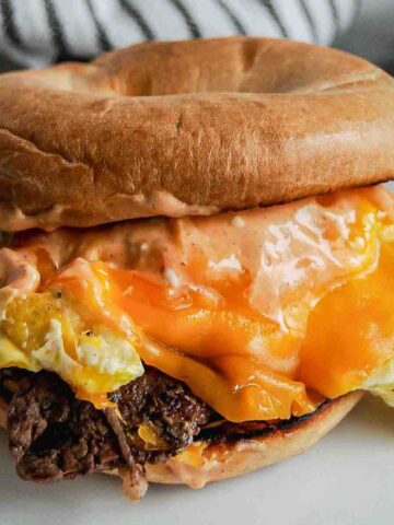 steak egg and cheese bagel with breakfast sauce on plate.