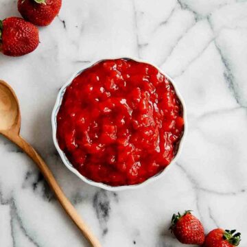 strawberry cake filling in bowl on countertop with wooden spoon and fresh strawberries to the side.