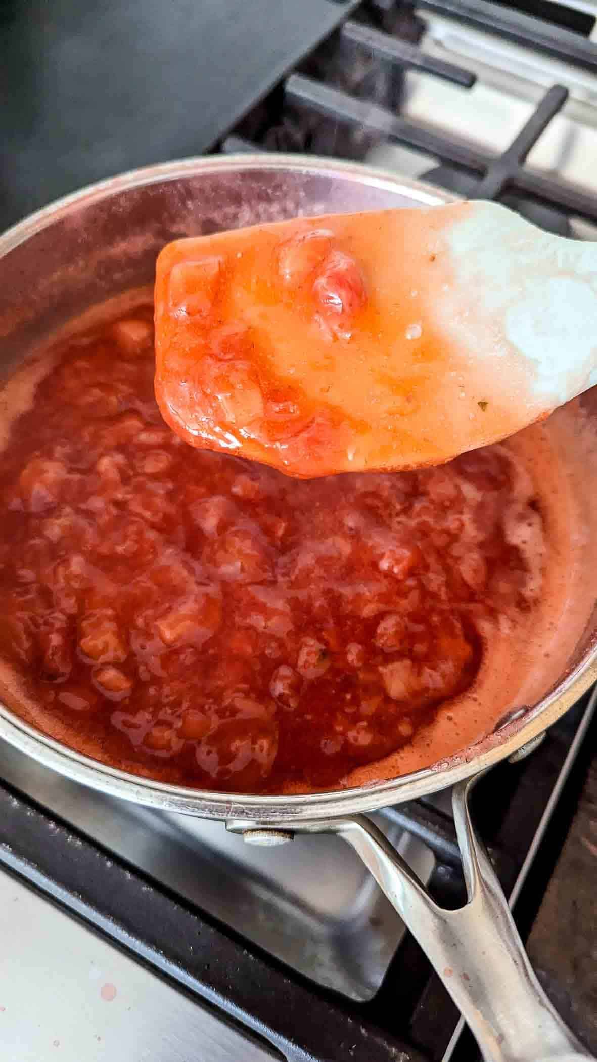 strawberry sauce thickening in saucepan, clinging to the back of a spatula.