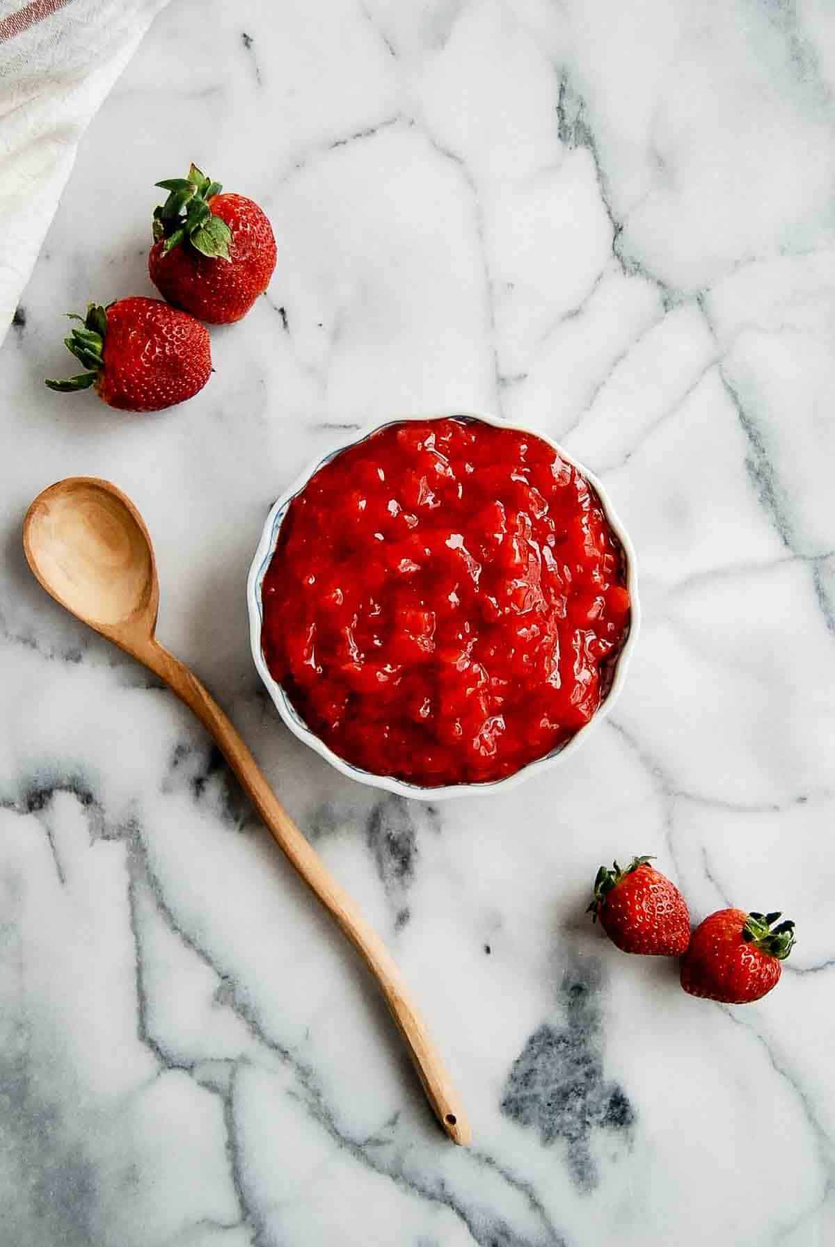 strawberry filling for cakes in bowl on countertop with wooden spoon to the side.