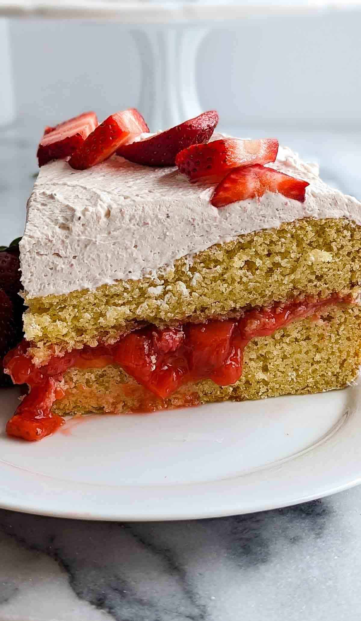 side view of strawberry vanilla cake with strawberry filling and strawberry whipped cream icing on top.