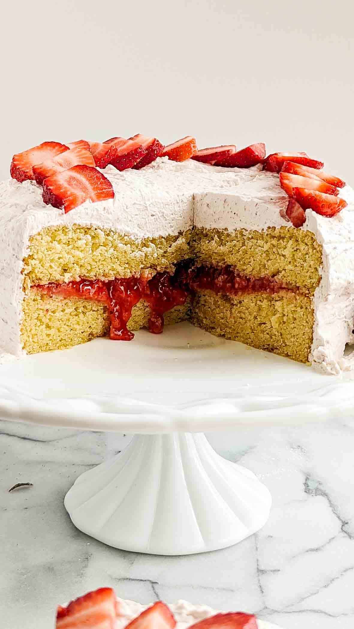 strawberry vanilla cake with strawberry filling and strawberry whipped cream on cake stand with portion cut out.